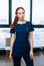 Vertical portrait of serious redhead female doctor wearing medical dark uniform looking at camera standing on background Royalty Free Stock Photo