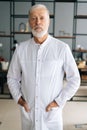 Vertical portrait of serious senior adult male doctor in white medical uniform standing in hospital office, looking at Royalty Free Stock Photo