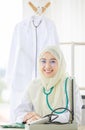 Vertical portrait shot of an attractive smiling adult Muslim woman wearing cream hijab, stethoscope, and eyeglasses looking at the Royalty Free Stock Photo