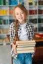 Vertical portrait of smiling elementary child school girl holding stack of books in library at school, looking at camera Royalty Free Stock Photo