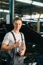 Vertical portrait of smiling handsome young mechanic male wearing uniform holding special key ratchet wrench showing Royalty Free Stock Photo