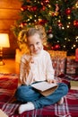 Vertical portrait of smiling little blonde curly girl writing letter to Santa Claus sitting on floor on background of Royalty Free Stock Photo