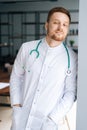 Vertical portrait of smiling male doctor wearing white medical uniform standing with stethoscope in hospital office Royalty Free Stock Photo