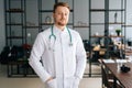 Vertical portrait of smiling male doctor wearing white medical uniform standing with stethoscope in hospital office Royalty Free Stock Photo