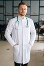 Vertical portrait of smiling male doctor wearing white medical uniform standing with stethoscope in hospital office Royalty Free Stock Photo