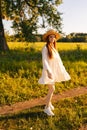 Vertical portrait of smiling red-haired young woman in straw hat and white dress standing posing looking at camera on Royalty Free Stock Photo