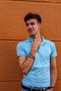 Vertical portrait of smiling young man in blue polo shirt with hand on shirt collar on orange background Royalty Free Stock Photo