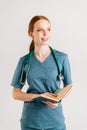 Vertical portrait of smiling young woman physicianin green uniform with stethoscope holding medical book standing and Royalty Free Stock Photo