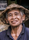 Vertical portrait of South Asian Balinese senior man wearing a traditional Balinese cone-shaped hat. An elderly man