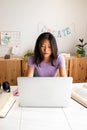 Vertical portrait of teenage female Asian high school student doing homework and studying at home using laptop. Royalty Free Stock Photo