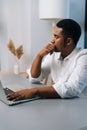 Vertical portrait of thoughtful black businessman working on business strategy on laptop sitting at desk, thinking Royalty Free Stock Photo