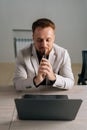 Vertical portrait of thoughtful businessman in suit holding smartphone sitting at office desk with laptop computer Royalty Free Stock Photo