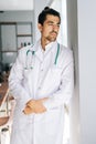 Vertical portrait of thoughtful male doctor wearing white medical uniform standing with stethoscope in hospital office Royalty Free Stock Photo