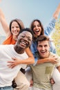 Vertical portrait of two multiracial young friends giving piggyback ride to his girlfriends. A group of happy people Royalty Free Stock Photo