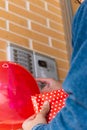 Vertical portrait of unrecognizable man whit gift and love balloon pressing the doorbell buttons at home to give her partner a