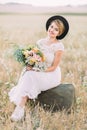 The vertical portrait of the vintage dressed bride holding the wedding bouquet of the colourful flowers, sitting on the