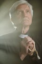 Vertical white haired senior priest praying with rosary in serene god rays