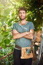 Vertical portrait of young attractive bearded dark-skinned farmer in blue t-shirt with garden tools holding hands