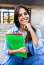 Vertical portrait of young beautiful female college student sitting outside university building looking at camera. Royalty Free Stock Photo