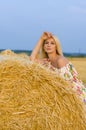 Vertical portrait of a young blonde near a haystack on a background of sky and field