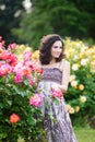 A vertical portrait of young Caucasian woman with dark brown curly hair near pink rose bushes, looking to her left, smiling with Royalty Free Stock Photo