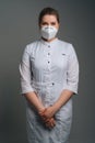 Vertical portrait of young female doctor wearing medical coat and protective face mask standing on dark isolated Royalty Free Stock Photo