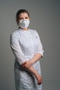 Vertical portrait of young female doctor wearing medical coat and protective face mask standing on dark isolated Royalty Free Stock Photo