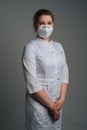 Vertical portrait of young female doctor wearing medical coat and protective face mask standing on dark isolated Royalty Free Stock Photo