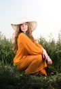 Vertical portrait of a young woman sitting in a field. Straw hat