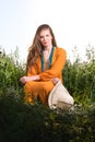 Vertical portrait of a young woman sitting in tall grass. Red dress Royalty Free Stock Photo