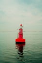 Vertical of a red beacon floating in the sea with the sky and the horizon in the background