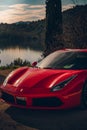 Vertical of a red Ferrari parked against a beautiful sight of a lake at sunset