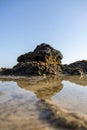 Vertical of the reflection of a rugged rock made of lava on the shallow water of a small lake Royalty Free Stock Photo