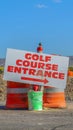 Vertical Road under construction with golf course entrance sign and traffic barrels