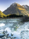 Vertical rocky mountain landscape in early winter with snow-capped peaks and colorful forest and a mountain stream in the foregrou