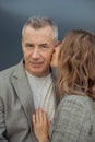 Vertical romantic couple of two mature gray haired man and young woman kissing to cheek, stroking on gray background Royalty Free Stock Photo