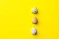 Vertical row of multicolored speckled chocolate eggs on bright yellow background. Easter greeting card poster banner Royalty Free Stock Photo