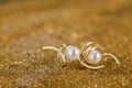 Vertical selective focus closeup of gold pair of earrings with pearl on a gold background