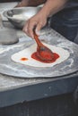 Vertical selective focus shot of a hand saucing the dough of pizza with a wooden spoon Royalty Free Stock Photo
