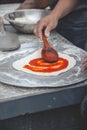 Vertical selective focus shot of a hand saucing the dough of pizza with a wooden spoon Royalty Free Stock Photo