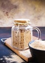 Vertical shot of active sourdough starter in glass jar. Rye leaven for bread and cup of flour on wooden cutting board on black and