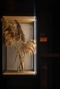 Vertical shot of artificial sheaves of wheat in a glass vase on a shelf with lights