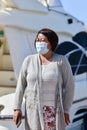 Vertical shot of an Asian female in a medical mask standing against a boat