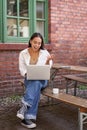 Vertical shot of asian girl with laptop, talking on video call, chatting online, sitting in cafe outdoors Royalty Free Stock Photo