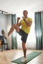 Vertical shot of athletic strong mature man in sportswear exercising at home on yoga mat in the living room