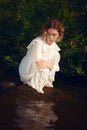 Vertical shot of an attractive Russian female in a beautiful white dress posing by the lake