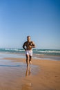 Vertical shot of an attractive topless man with tattoos running on a beach next to a sea