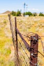 Vertical shot of a barbed-wire fence protecting a dry area with an old windmill in South Africa Royalty Free Stock Photo