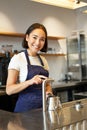 Vertical shot of barista, girl in coffee shop, pouring water in kettle, preparing order in cafe, smiling at camera Royalty Free Stock Photo