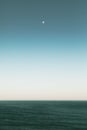 Vertical shot of a beautiful view of ocean under the moon in the blue sky Royalty Free Stock Photo